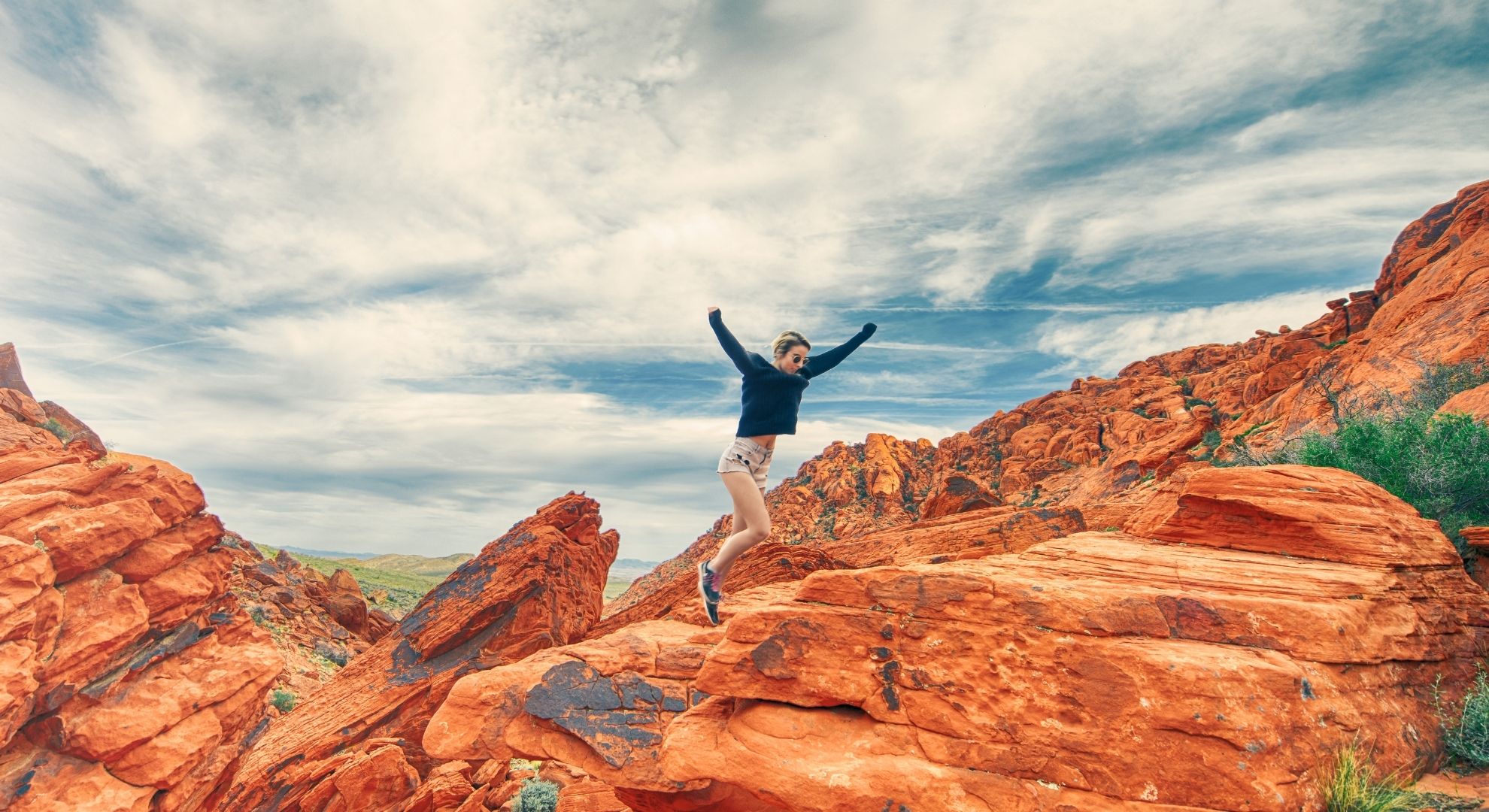 person leaps from rock to roc across sandstone landscape